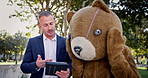 Business people, tablet and discussion of team at park outdoor in funny teddy bear costume. Technology, meeting and collaboration of consultants planning or brainstorming ideas with mascot in garden