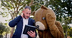 Business people, tablet and team planning outdoor at park in funny teddy bear costume. Technology, meeting and collaboration of consultants in brainstorming discussion, mistake or fail with mascot