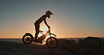 Man, hill and motorbike with sunset for travel, adventure or riding on rocks, training or extreme sports. Biker silhouette or person in safety helmet and bike for journey by ocean or sea in Australia