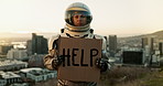 Astronaut, city and billboard with sign for message, alert or signal help on news or note to people on earth. Portrait of traveler with board for notification, awareness or protest in an urban town