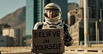 Astronaut, city and billboard with sign for motivation, message or note to people on earth. Portrait of space traveler showing board or notification for courage, humanity or awareness in urban town