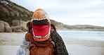 Happy, kids and outdoor with dinosaur costume on beach and hug person as crazy character. Trex, outfit and children embrace funny inflatable monster with love and care on holiday or vacation 