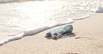Beach, ocean and plastic bottle in sand for pollution, litter and trash in sea for global warming crisis. Nature, climate change and closeup of garbage in sea to reduce waste, recycling and cleaning