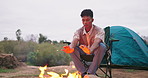 Camping, fire and man warm hands in nature for adventure, outdoor holiday and vacation. Travel, weekend and person relax by bonfire, flames and heat with tent on campsite, countryside and woods