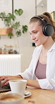 Woman, laptop and headphones in coffee shop for typing for remote work at online media agency. Girl, person or writer with computer, drink and smile with music for editing process in trendy cafeteria