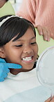 Dental care, oral hygiene and mirror with indian girl at dentist in chair for consulting or checkup. Appointment, healthcare and medical with happy child patient in clinic for teeth whitening