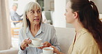 Senior mother, daughter and coffee in retirement home with conversation, visit or chat on sofa in morning. Women, relax and drink with tea cup, care and bonding for connection at breakfast in lounge