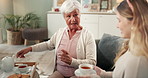 Senior mom, woman and tea in living room with helping hand, care and conversation for visit in family home. Elderly mother, daughter and relax on couch in lounge with warm drink with talk for memory