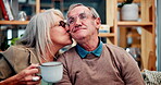 Senior, couple and kiss on sofa with coffee in morning with conversation, love and happiness with contentment. Mature, man and woman relax together in home with warm beverage for comfort and bonding.