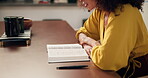 Woman, book and reading a bible in home for worship, gratitude and information on God in living room. Christianity, person and praying for faith, belief and spirituality by table in lounge of house