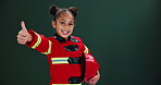 Children, thumbs up or girl in fireman suit in studio with feedback, review or emoji hand motivation on green background. Thank you, face or kid in firefighter costume for halloween, dream or fantasy