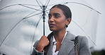 Indian woman, rain and waiting with umbrella for transport, business trip or commute to work in winter. Female person or employee on sidewalk in neighborhood with protection and looking for lift