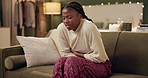 African woman, menstruation and stomach on sofa with pain, stress or cramps at night in living room. Girl, person and holding sore abdomen with virus, constipation or ibs on lounge couch in apartment
