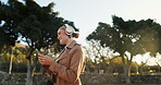 Woman, business and headphones with cellphone in park for work commute, streaming or podcast. Female person, walking and happiness in urban city for morning travel with music, entertainment or audio