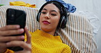 Happy girl, relax and lying with phone on bed for social media, browsing or listening to music above at home. Top view of young female person with headphones on mobile smartphone for audio in bedroom