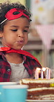 Boy, blow candles and cake at kindergarten, happy or celebration with birthday party, flame and food. Child, classroom and idea for wish, dessert and superhero mask for event at preschool academy