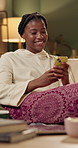 African woman, phone and texting on sofa in home with smile, thinking or check notification in living room. Girl, smartphone and happy in night with pajamas on couch with reading post on social media