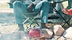 Campsite, nature and hand with kettle on fire for morning coffee, warm drink or beverage in forest. Camping, travel and woman by bonfire for tea in woods for holiday, winter adventure or relax