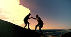 People, holding hands and fitness in sunset at beach with help on rocks, clouds and outdoor together. Men, support and lift by ocean, sea and silhouette with training, exercise or workout in summer