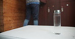 Fitness, man and back with water bottle in gym dressing room before workout for drink and hydration. Male person, health and balanced diet with glass container for nutrition, and electrolytes