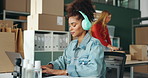 African woman, laptop and logistics at startup, typing and headphones by boxes, shelf or supply chain in office. Person, employee and computer for music, storage and invoice admin for shipping job