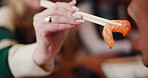 Woman, hands and feeding shrimp with chopsticks for dinner, date or eating at indoor restaurant. Closeup of female person giving seafood to friend for taste, salmon or nutrition at cafeteria together