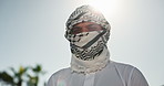 Blue sky, Muslim and face of man in city with traditional head wrap for culture, belief and religion. Islamic faith, Arabic and portrait of person for Eid, Ramadan Kareem or hajj in Saudi Arabia