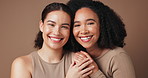 Friends, face and laughing in studio for skincare, makeup and embrace on brown background. Women, portrait and confident in dermatology or foundation glow, facial treatment and support for beauty