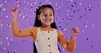 Girl, face and dancing with confetti in studio for playful fun, excited and winner of kid competition. Happy, little person and smile on purple background for birthday, surprise and celebration