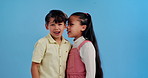 Sneaky children, whisper and shock with secret in studio for gossip, trust or friendship on a blue background. Little boy, girl or kids telling rumour in ear with surprise or reaction for news or lie