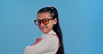 Crossed arms, sunglasses and face of child in studio for confidence, trendy style and cool accessories. Happy, smile and portrait of girl with shades for joy, pride and fashion on blue background