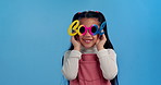 Fashion, sunglasses and face of girl in studio for confidence, funky style and cool accessories. Happy, smile and portrait of young girl with eyewear for joy, pride and cute on blue background