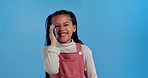 Happy girl, child and laughing with phone call for funny conversation, gossip or chat in studio on a blue background. Portrait of young female person or little kid with smile on mobile smartphone