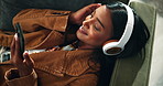 Happy woman, sofa and headphones with phone for music, playlist or audio on holiday at home. Young female person lying on couch or enjoying song, album or podcast with headset in living room at house