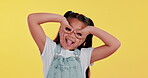 Funny, face and girl child in studio with playful eye gesture, positive attitude and happy development. Playing, comedy and portrait of crazy kid with games, growth and self love on yellow background