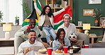 Group, people and celebration on sofa watching tv for soccer, world cup or event in living room. South African flag, diversity and friends with alcohol, happiness or goal from football team in home