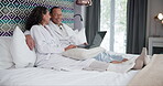 Couple, laptop and talking in bedroom of hotel with laughing, comedy movie or watching funny video in robes. People, happy and technology on bed of accommodation for relax, holiday and conversation