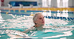 Senior woman, swimming and exercise in pool for health with aquatic sports, retirement and physiotherapy. Elderly lady, water gym and rehabilitation for arthritis, hydrotherapy and cardio workout