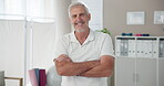 Mature man, arms crossed and physiotherapist in clinic with confidence for physical therapy and recovery service. Chiropractor portrait, person and happy at workplace for rehabilitation and wellness