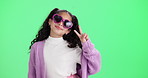 Girl, child and sunglasses with peace sign by green screen in studio with smile, face and icon by background. Kid, happy and v symbol with fashion, confident and trendy style with heart lens shades