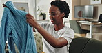 Black woman, folding clothes and cleaning house for laundry hygiene, tidy and fabric maintenance of hospitality service. Smile, female person and housekeeping with jersey, packing and organising home