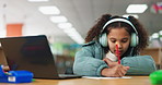 Girl, school and writing with laptop for education at library for online tutoring, project and assessment. Kid, elearning and serious with headphones for distance learning and child development