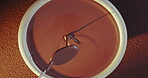 Hand, spoon and woman with chocolate in bowl for production, process and preparing for baking. Top view, cocoa and chocolatier with mixing of liquid for tempered ganache, texture or smooth ingredient