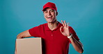 Delivery man, face and box with okay sign for success, product safety and courier services in studio. Portrait, trust or happy supply chain worker with package or distribution on blue background