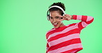 Woman, face and headphones with dancing by green screen for audio, streaming and listening to music. Happy, person and crazy with technology in studio for silent disco, party and sound experience