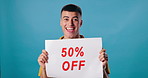 Poster, half discount and face of man in studio for 50 percent promotion, shopping and sign. Happy, advertising and portrait of person with banner for retail sale, deal and bargain on blue background