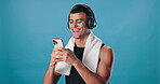 Man, cellphone and texting in studio with fitness, headphones and towel for workout. Happy athlete, mockup and technology with laugh, exercise and streaming podcast or music on blue studio background