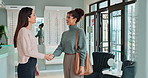 Smile, people and handshake in optometry store for welcome, customer service and eye care purchase. Sales assistant, women and hand gesture in shop for greeting, consultation and decision for glasses