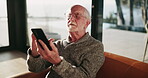 Online, mobile and elderly man on sofa for puzzle game, memory test or health website in living room. Scroll, glasses and senior person for browsing internet, reading ebook or retirement in home