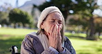 Senior woman, sick and sneezing with tissue in park for pollen allergies, flu virus and health risk. Elderly person, toilet paper and blowing nose in nature for sinus problem, hayfever and bacteria